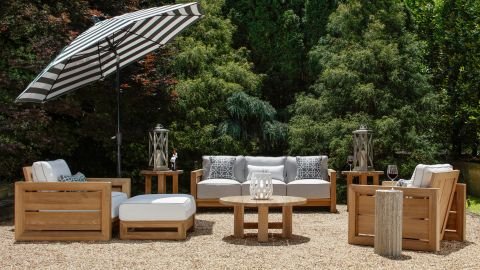 Elegant wooden outdoor furniture set with a black & white umbrella, placed amidst lush greenery for a cozy outdoor setting.